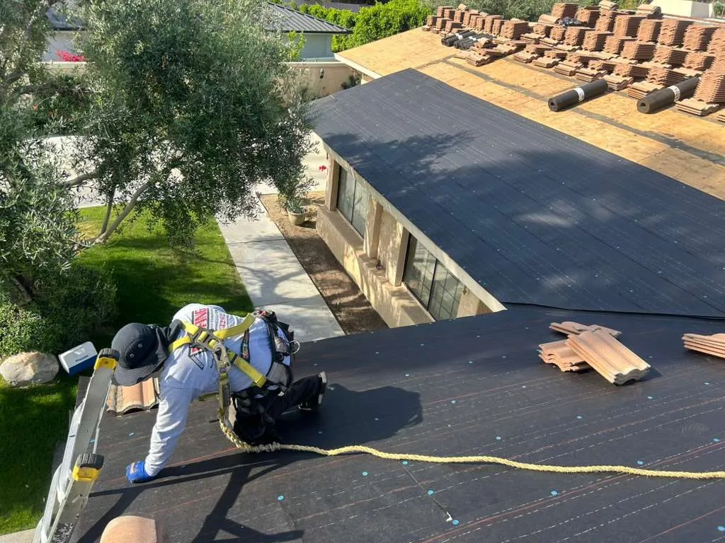 A Beaumont Roofing crew member, tied off and harnessed, prepping a residential tile re-roof in the Inland Empire.
